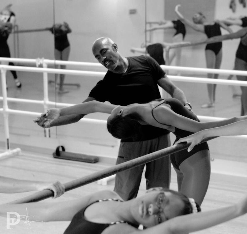 Bryant works with a young ballet dancer at the barre. He elongates her finger tips as she stretches back